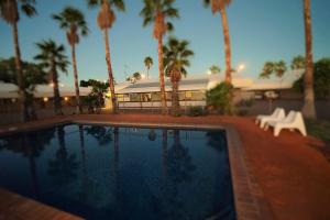a swimming pool with palm trees in front of a building at Bluestone Motor Inn in Tennant Creek