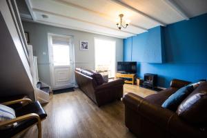 a living room with blue walls and leather furniture at Ploughmans Cottage, St Florence, Tenby in Saint Florence