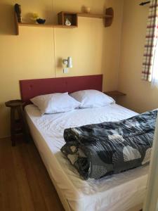 a bed with a red headboard and white sheets and pillows at Mobilhome (29) 4 pers St Martin aux Buneaux in Saint-Martin-aux-Buneaux