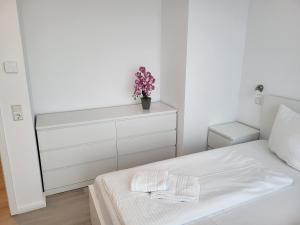 a white bedroom with a bed and a dresser with a plant at Der Landhof Möwe LH 103 in Stolpe