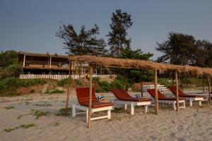 a group of chairs sitting under a straw umbrella on the beach at Woodpegger By The Beach, Mandrem in Mandrem