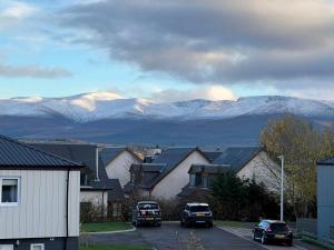 a town with cars parked on a street with snow covered mountains at Caledonia Place in Aviemore