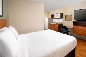a hotel room with a white bed and a kitchen at WoodSpring Suites Chicago Romeoville in Romeoville