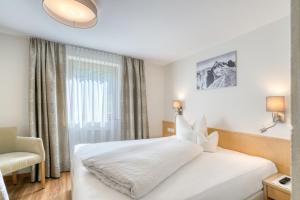 a bedroom with a white bed with a chair and a window at Landhaus Maria in Stuben am Arlberg