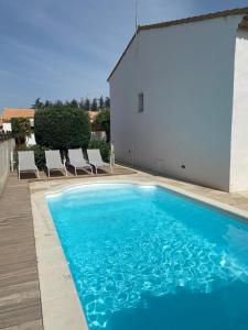 una piscina blu con sedie e un edificio bianco di Belle villa spacieuse avec piscine privée, 10 couchages,wifi, proche canal du midi et à 3 km de la mer LXPIN7 a Portiragnes