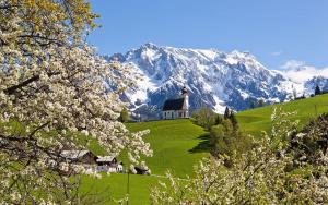 una chiesa su una collina con una montagna innevata di Leni's Mountain Appartements a Dienten am Hochkönig