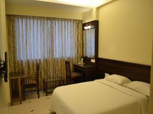 a bedroom with a bed and a desk and a window at Hotel GreenLand-Elegant in Kolhapur