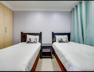 two beds in a small room with green curtains at The Sails Apartment in Durban