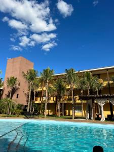 a swimming pool in front of a building with palm trees at Wakanda Hotel in Andradina