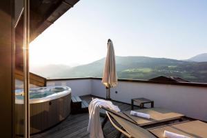 einen Balkon mit einer Badewanne, einem Stuhl und einem Sonnenschirm in der Unterkunft Granpanorama Hotel StephansHof in Villanders