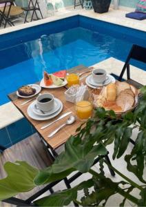 a table with breakfast food and drinks next to a swimming pool at Tô na Praia Juquehy Pousada in Juquei