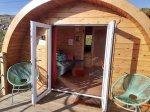 uma pequena casa com duas cadeiras e uma porta aberta em The Sleepy Crofter Glamping - Achiltibuie em Achiltibuie