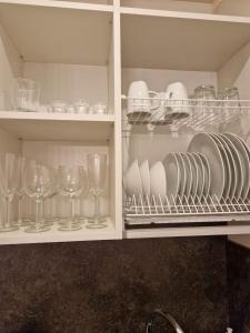 a cupboard with glasses and plates and wine glasses at Parko nauji apartamentai in Panevėžys