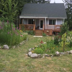 una casa con terraza y un patio con flores en Cozy ,artistic cottage in a garden setting close to the beach and hiking trails., en Powell River