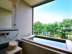 a bathroom with a bath tub with a large window at Jodogahama Park Hotel in Miyako