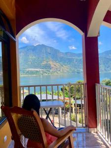 eine Person auf einem Stuhl auf einem Balkon mit Blick auf das Wasser in der Unterkunft Hotel Adulam in San Pedro La Laguna