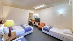 a hotel room with two beds and a desk at Goulburn Central Motel in Goulburn