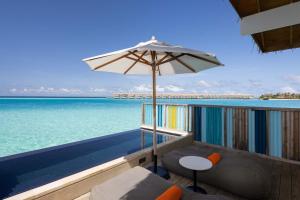 a balcony with an umbrella and chairs and the ocean at Hard Rock Hotel Maldives in South Male Atoll