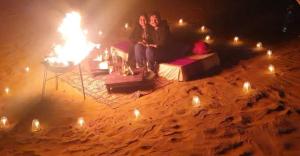 two people sitting on a couch in front of a fire at Jodhpur Camel Safari & Overnight Stay In Desert Jodhpur NotOnMap in Jodhpur