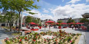 una plaza con mesas, sombrillas rojas y flores en Charmante petite maison en Cholet