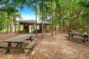 two picnic tables in front of a cabin in the woods at Emohruo Rainbow Shores - 3 Br Resort Apartment in Rainbow Beach