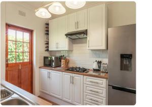 a kitchen with white cabinets and a stainless steel refrigerator at Meerendal Cottage-Affordable Luxury,Private Pool in Cape Town