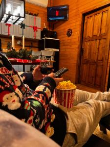 a person sitting on a couch holding a glass of wine and popcorn at Montebello Chalet in Porumbacu de Sus