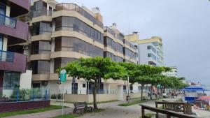 un edificio en una calle de la ciudad con bancos y árboles en Apto pé na areia em Meia Praia Itapema, 3 dormitórios, en Itapema