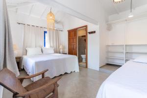 a white bedroom with a bed and a chair at Arandu Casa Hotel Quadrado in Trancoso