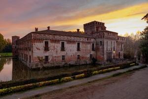 un vecchio edificio in mattoni seduto in acqua al tramonto di Agriturismo Padernello a Borgo San Giacomo