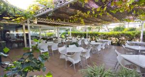 un restaurante con mesas blancas, sillas y plantas en Campomar Playa, en El Puerto de Santa María