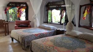 a bedroom with two beds and a chair and windows at La Quinta Orquídea in Puerto Morelos