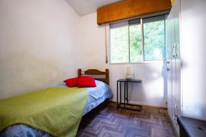 Schlafzimmer mit einem Bett mit einem roten Kissen und einem Fenster in der Unterkunft Hermoso apartamento en el centro de Atlántida in Atlántida