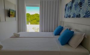 una camera con 2 letti con cuscini blu e una finestra di Casa em condomínio em Arraial D'ajuda a Porto Seguro