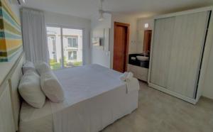 una camera bianca con un grande letto bianco con cuscini di Casa em condomínio em Arraial D'ajuda a Porto Seguro