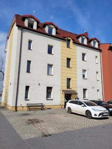 un coche blanco estacionado frente a un gran edificio en Apartamenty Radiostacja, z miejscem parkingowym en Gliwice