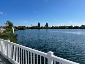 a view of a lake with a white fence at Chichester Lakeside Holiday Park Lakefront Lodge in Merston