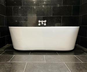 een wit bad in een zwart betegelde badkamer bij The Wrea Head Hall Country House Hotel & Restaurant in Scarborough