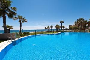 uma grande piscina azul com palmeiras e o oceano em Mar Azul ApartHotel em Estepona