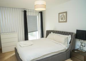 LUXURY 2 BED WOOLWICH ARSENAL Apartment في لندن: غرفة نوم بسرير وملاءات بيضاء ونافذة