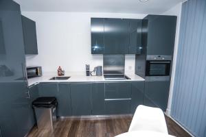 LUXURY 2 BED WOOLWICH ARSENAL Apartment في لندن: مطبخ مع خزائن زرقاء داكنة وعدادات بيضاء