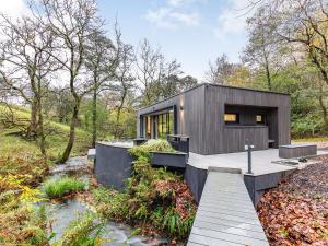 een klein zwart huis in het bos met een houten terras bij The Pump House Lodge in Elslack