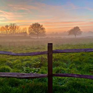 una valla de madera en un campo con un amanecer nublado en Quality Oak Barn with Hot Tub and Parking en Bramley