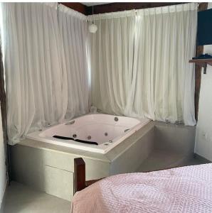 a bath tub in a room with curtains and a bed at Pousada Canto da Lua in Nova Lima