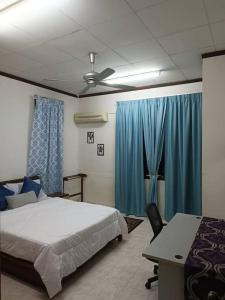 a bedroom with a bed and a table and blue curtains at Cozy house with free parking near Utm, Legoland in Skudai