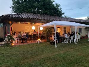 eine Gruppe von Menschen, die auf einer Terrasse unter einem weißen Zelt sitzen in der Unterkunft Les Tournesols in Sariac-Magnoac