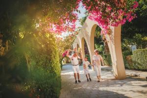 a family walking under an archway with pink flowers at Rufus Brand New Caesar Resort & Spa 1 Bedroom Apartment with big terrace in Iskele