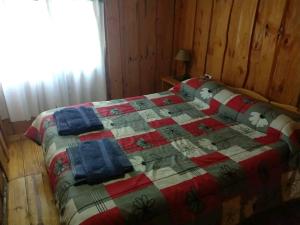 Una cama con edredón en una habitación en Murmullos del bosque en Lago Puelo