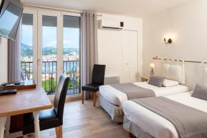 a hotel room with two beds and a desk and a window at Le Catalan in Banyuls-sur-Mer