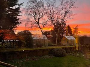 zwei Gewächshäuser in einem Garten mit Sonnenuntergang im Hintergrund in der Unterkunft The Old Station, Station House, Snettisham Norfolk in Snettisham